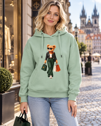 Žena v šalvějové mikině Shopping Is My Cardio s medvídkem a nákupními taškami před výlohou v Praze.