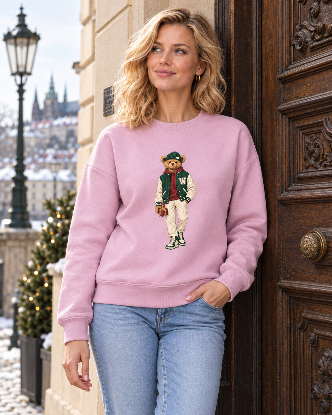 Blonde woman in a pink Winter Club bear crewneck sweatshirt at a wooden entrance in Prague.